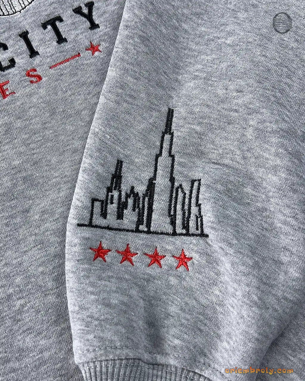 Close-up of custom sleeve embroidery featuring the Chicago city skyline and four red stars on a grey sweater sleeve