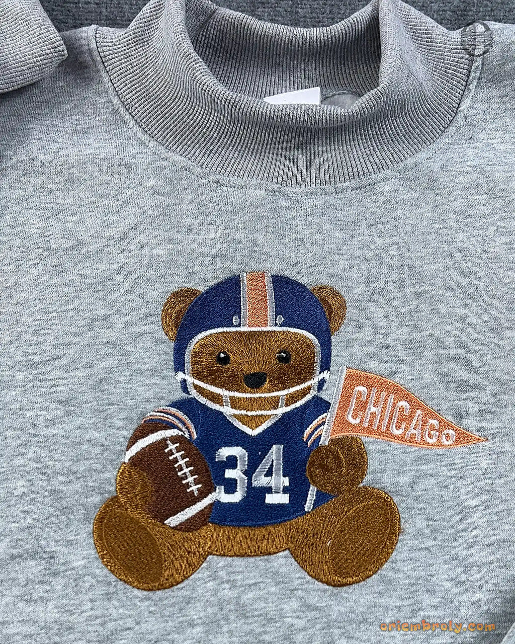 Close-up of Chicago football teddy bear embroidery wearing number 34 jersey and holding a orange Chicago pennant flag on a grey sweater