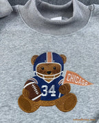 Close-up of Chicago football teddy bear embroidery wearing number 34 jersey and holding a orange Chicago pennant flag on a grey sweater