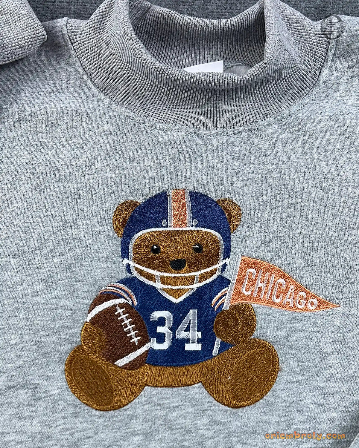 Close-up of Chicago football teddy bear embroidery wearing number 34 jersey and holding a orange Chicago pennant flag on a grey sweater