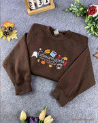 Overview flat lay of a chocolate brown Gilmore Girls embroidered crewneck sweatshirt with fall foliage decor