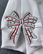 Close-up of red and green striped Christmas ribbon bow embroidered on the left sleeve of a white sweatshirt