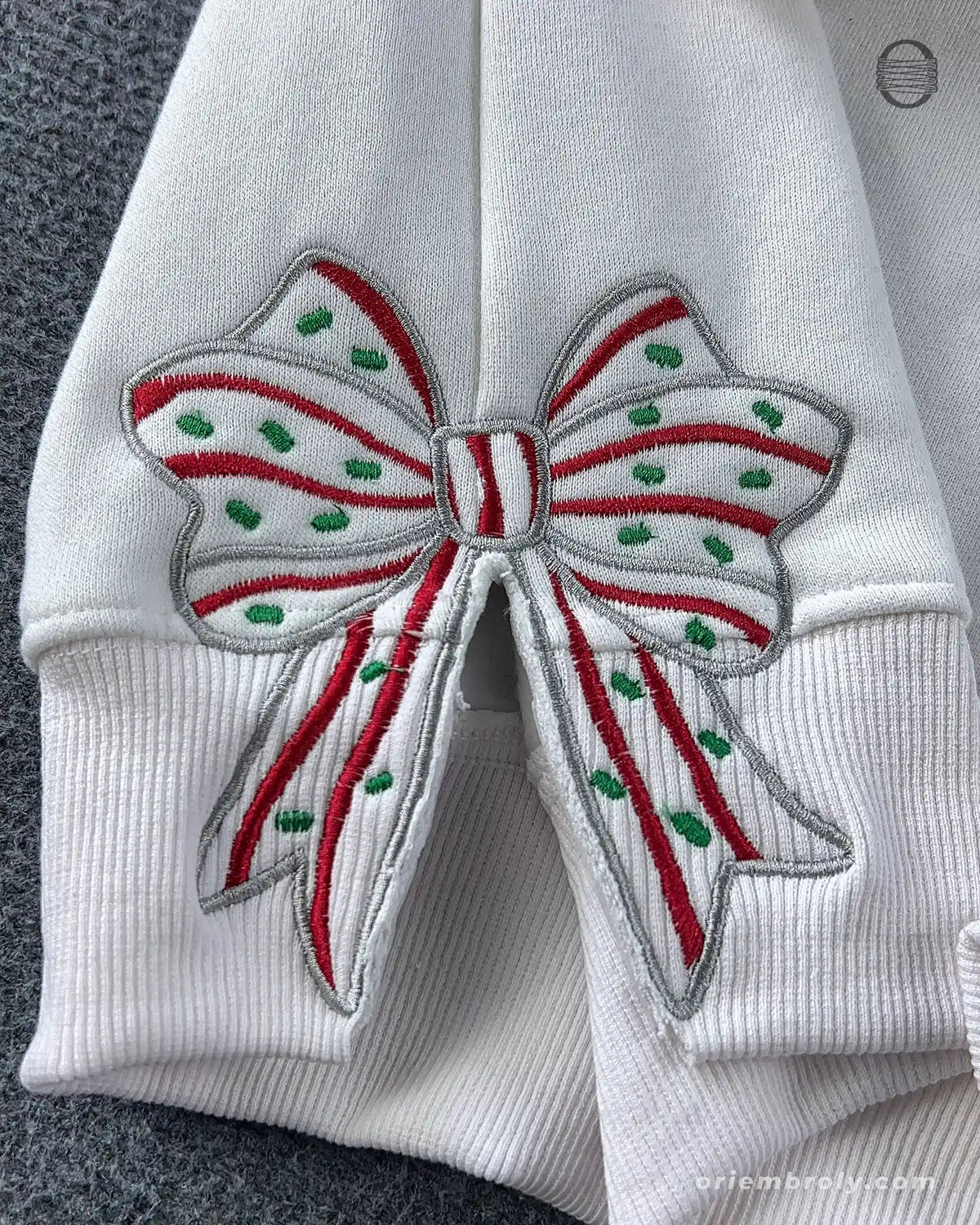 Close-up of red and green striped Christmas ribbon bow embroidered on the left sleeve of a white sweatshirt
