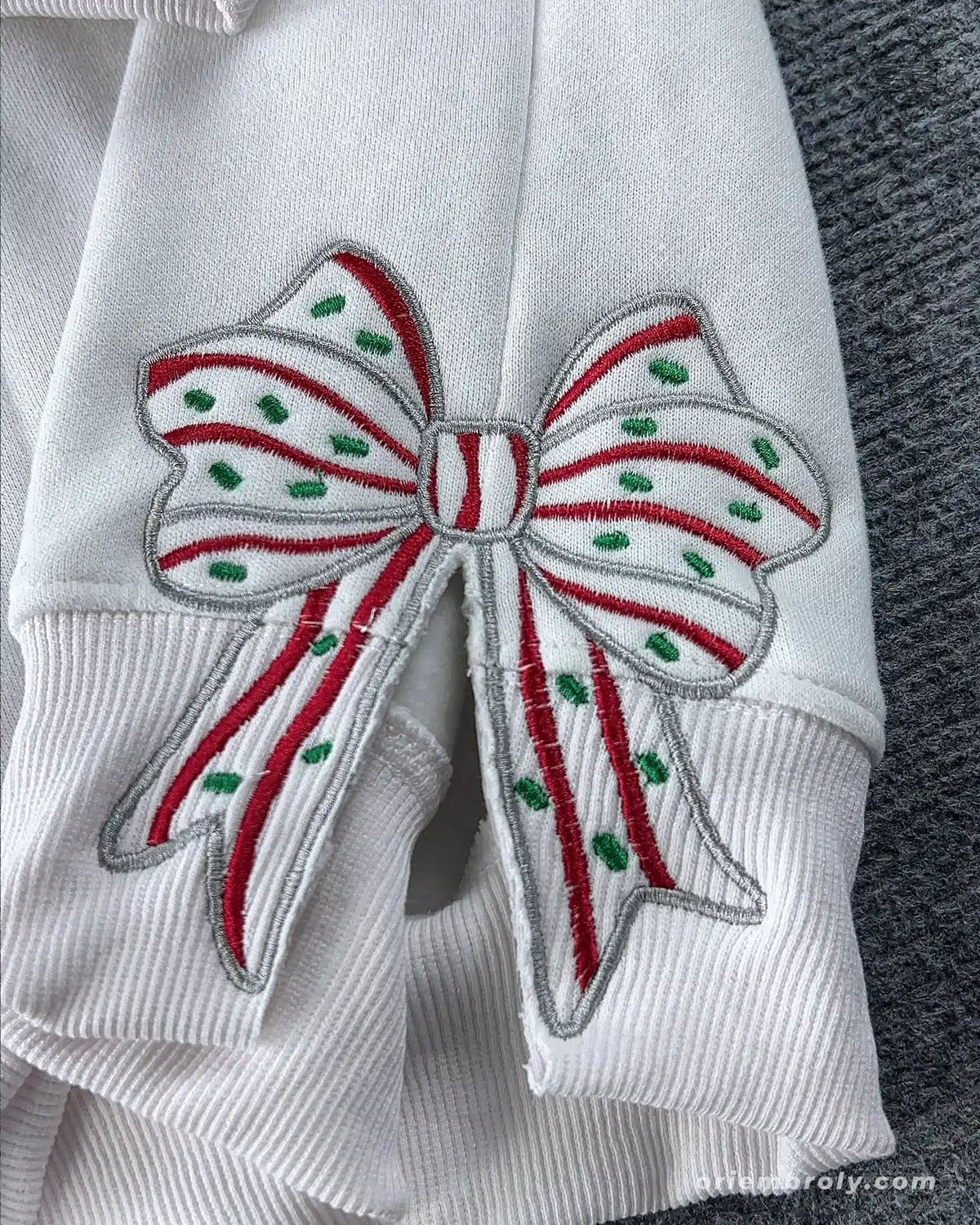 Close-up of festive Christmas bow embroidery on the right sleeve of a white crewneck sweater