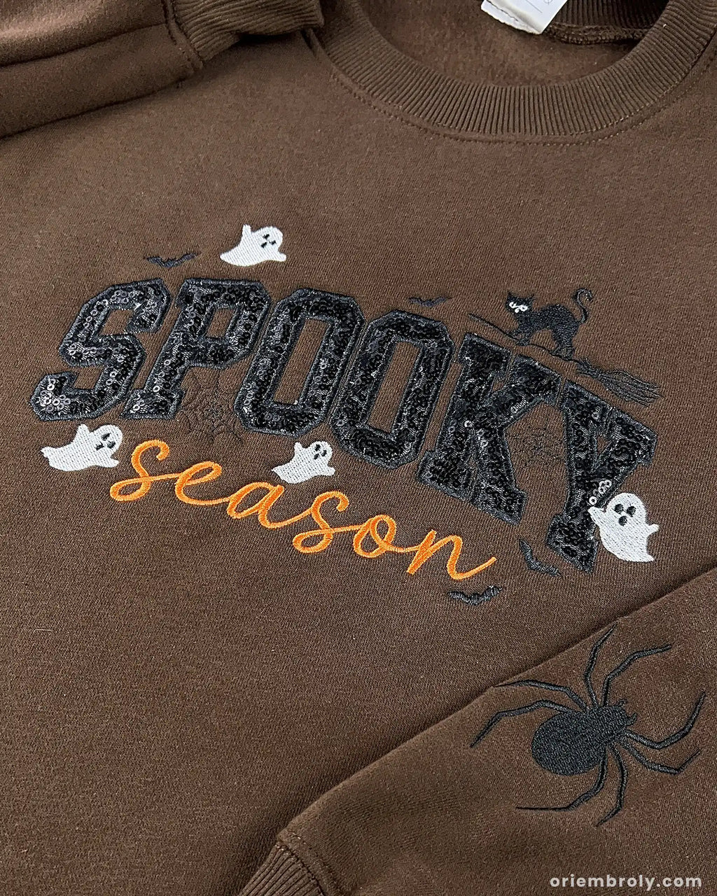 Close-up view of dark brown spooky season embroidered sweatshirt featuring black cat, ghosts, and sequined typography.