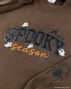 Close-up view of dark brown spooky season embroidered sweatshirt featuring black cat, ghosts, and sequined typography.