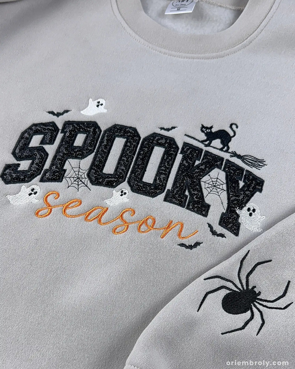 Front view of model wearing heather grey spooky season embroidered sweatshirt with black sequin letters.