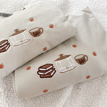 Folded fabric with embroidered designs of a house, cup, and sandwich on a textured surface.