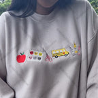 Gray sweatshirt with various embroidered items including an apple, school bus, and scissors.