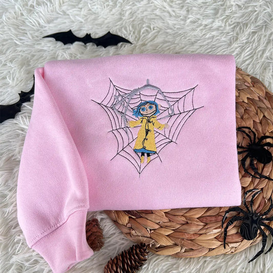 Pink sweatshirt with a spider web and character design on a textured surface with decorative elements.