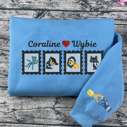 Folded blue sweatshirt with character illustrations and 'Coraline Wybie' text on a wooden surface
