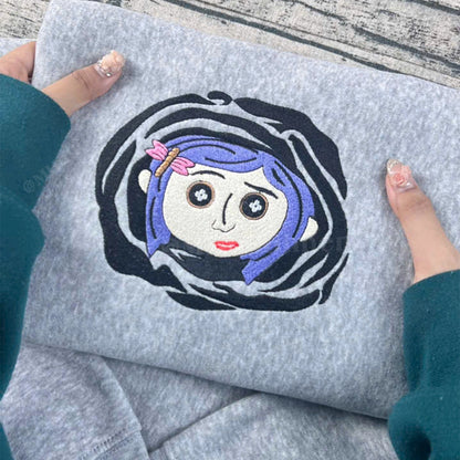 Gray sweatshirt with an embroidered design of a character with blue hair and a pink bow.