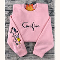 Pink sweatshirt with 'Coraline' design on a wooden surface