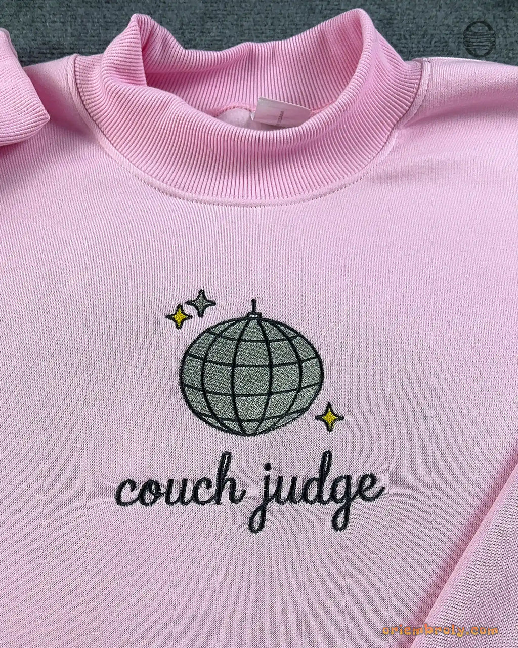 Close-up of silver disco ball with gold sparkles and Couch Judge cursive embroidery on a light pink sweater