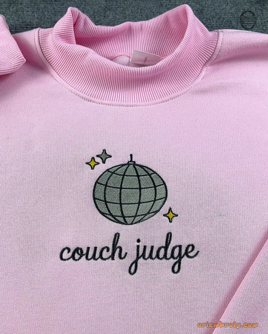Close-up of silver disco ball with gold sparkles and Couch Judge cursive embroidery on a light pink sweater