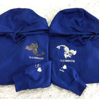 Two blue hoodies with embroidered designs on a textured surface