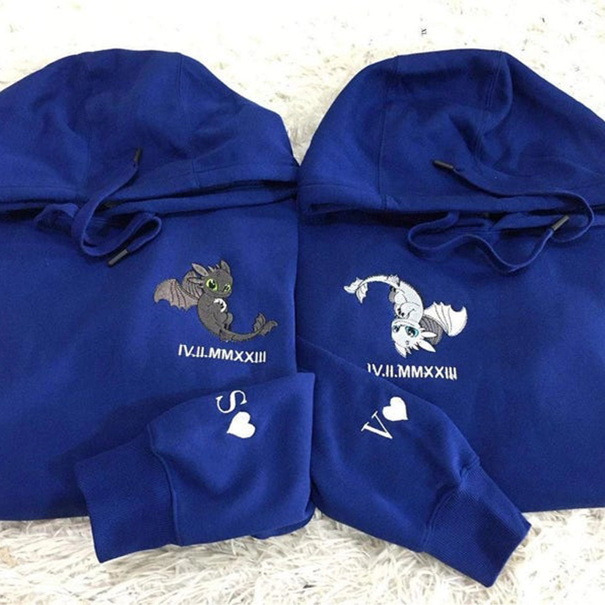 Two blue hoodies with embroidered designs on a textured surface