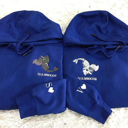 Two blue hoodies with embroidered designs on a textured surface