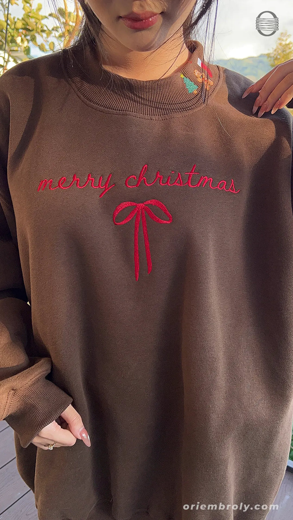 Front view of model wearing a chocolate brown Christmas sweatshirt showing red Merry Christmas script and bow embroidery