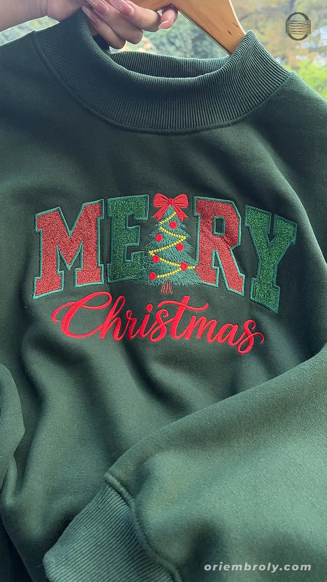 Overview of forest green Christmas embroidered crewneck sweater with red Merry Christmas text in natural lighting