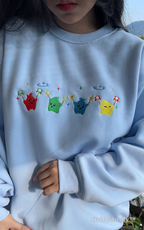 Cozy gaming apparel - Light blue sweatshirt with cute rainbow Junimos, ideal for cozy game nights.