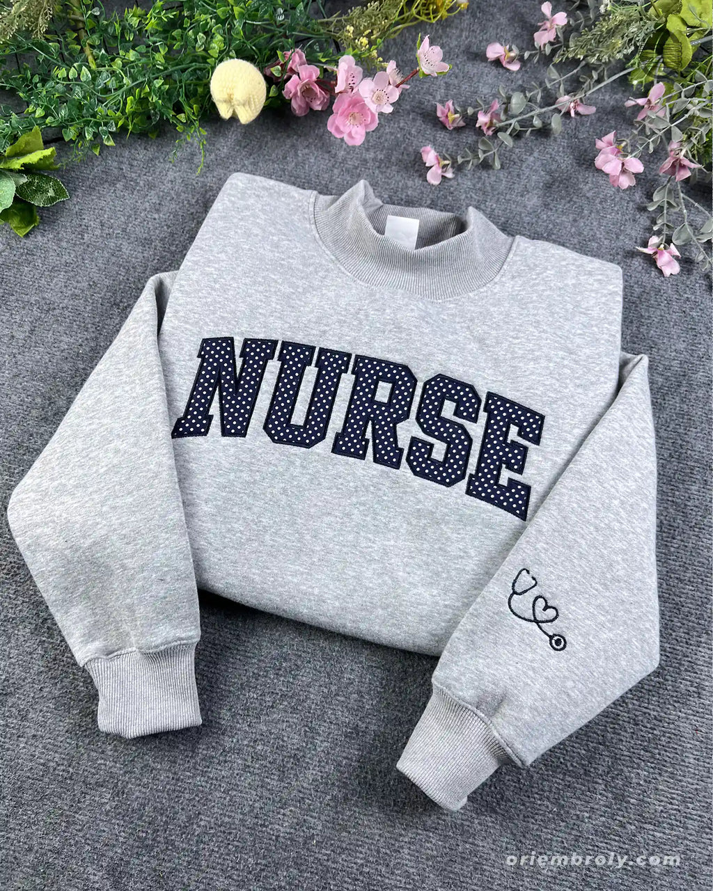 Overview of a sport grey nurse embroidered crewneck sweater featuring varsity block letters and medical stethoscope sleeve embroidery