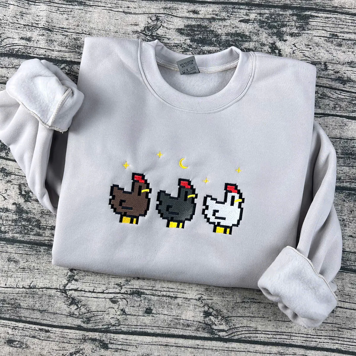 White sweatshirt with pixelated chicken designs on a wooden surface