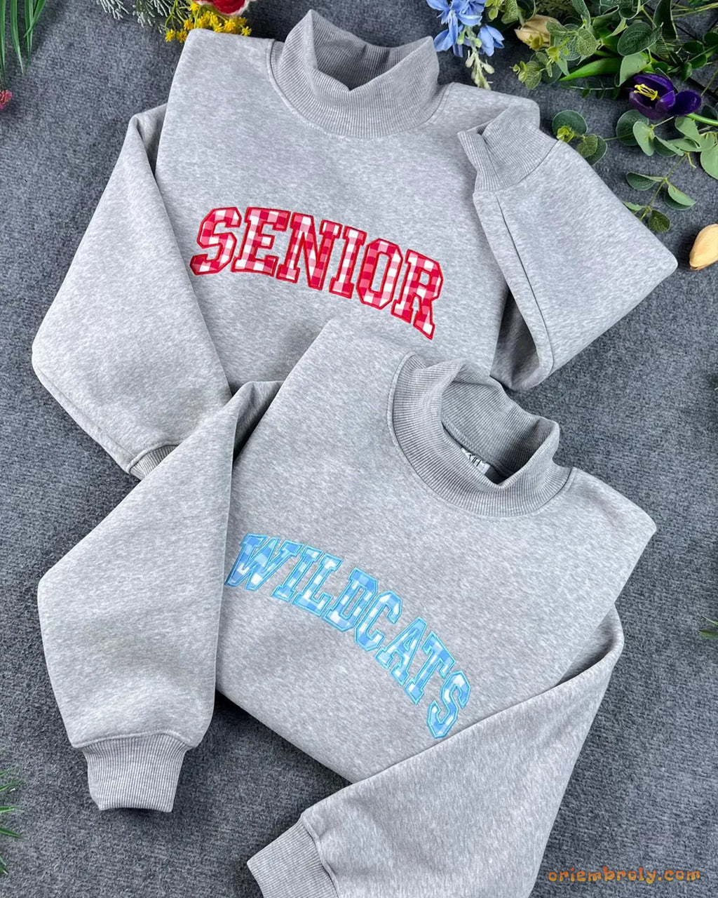 Stack of grey mock neck sweatshirts with custom red and blue embroidered applique letters
