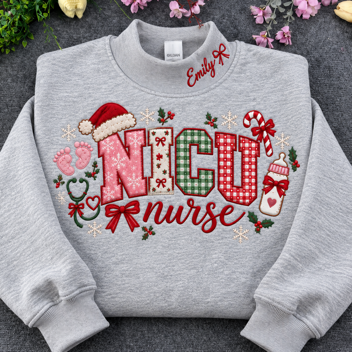 Flat lay of a sport grey crewneck sweatshirt embroidered with Christmas NICU nurse applique letters, santa hat, baby footprints, and custom collar name