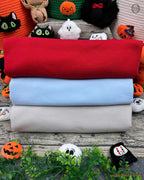 Stack of folded mock neck sweatshirts in red, light blue, and white with Halloween decor