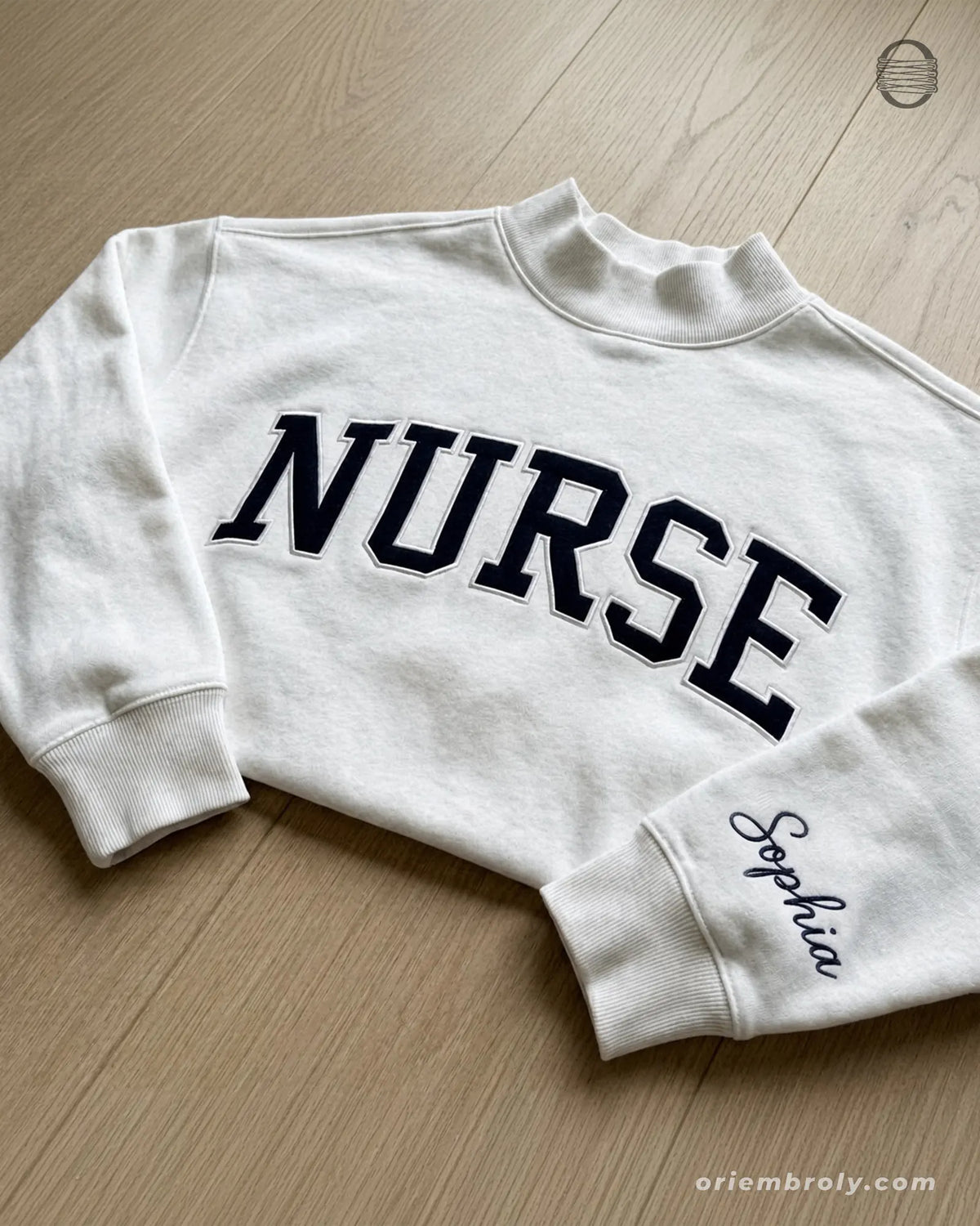 Flat lay of a white crewneck sweatshirt with varsity nurse chest embroidery and personalized name on sleeve