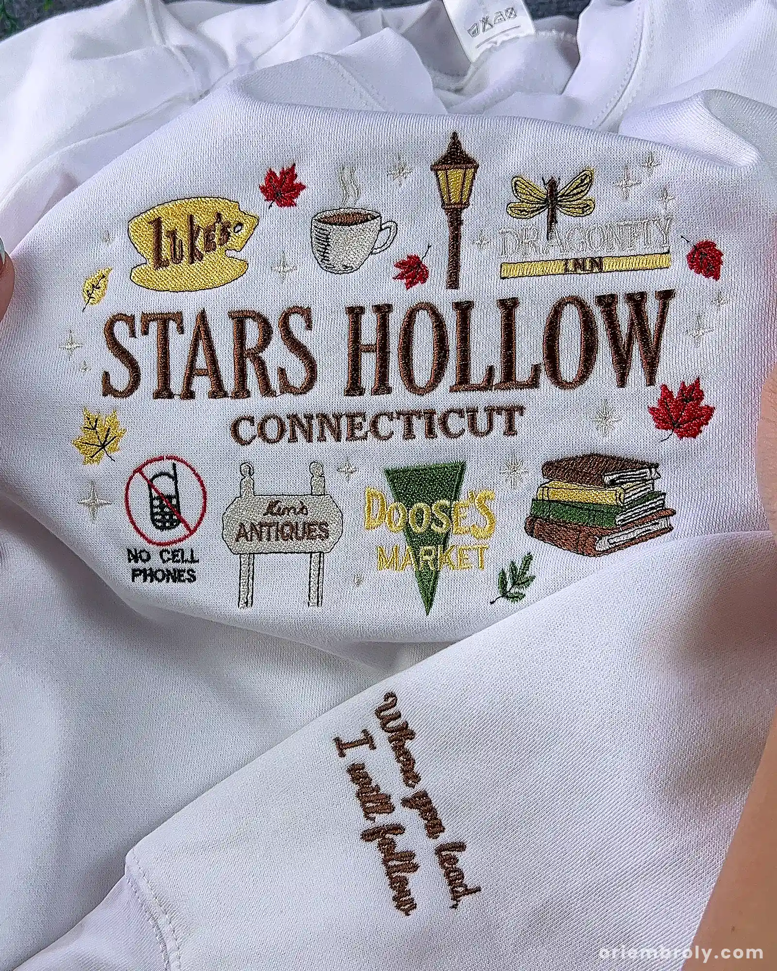 Detailed view of custom embroidered text quote on the sleeve of a white Stars Hollow Gilmore Girls sweatshirt.