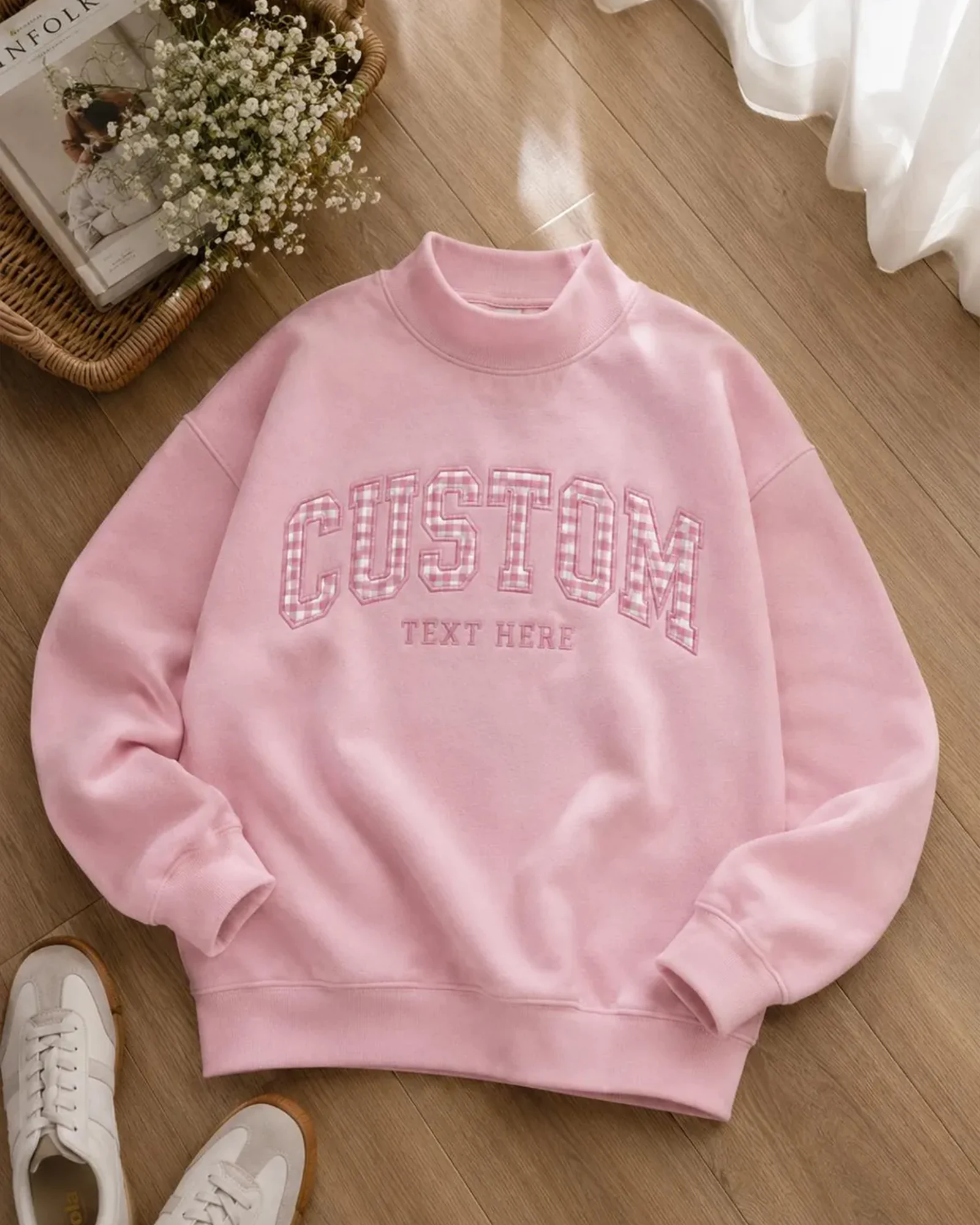 Light pink mock neck sweatshirt with custom embroidered text flat lay on wooden floor