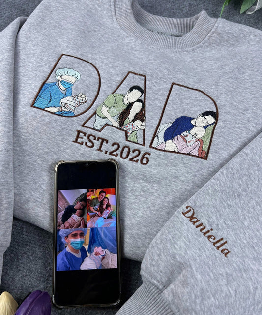Gray sweatshirt with embroidered designs and text, next to a smartphone displaying a family photo.