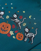Close-up of fine embroidery details showing a skeleton cat balancing on an orange pumpkin with colorful fall leaves.
