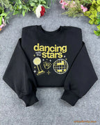 Flat lay of a black crewneck sweatshirt embroidered with gold Dancing with the Stars text, trophy, and mirrorball