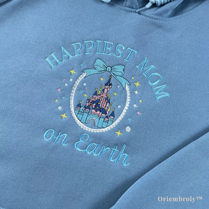 Close-up of premium satin stitch embroidery showing a pink and purple fairytale castle within a pearl-like circular frame on a soft blue hoodie. Durable, high-density thread work