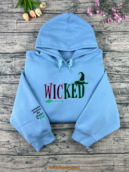 Light blue hoodie with 'WICKED' text on a wooden surface with flowers.