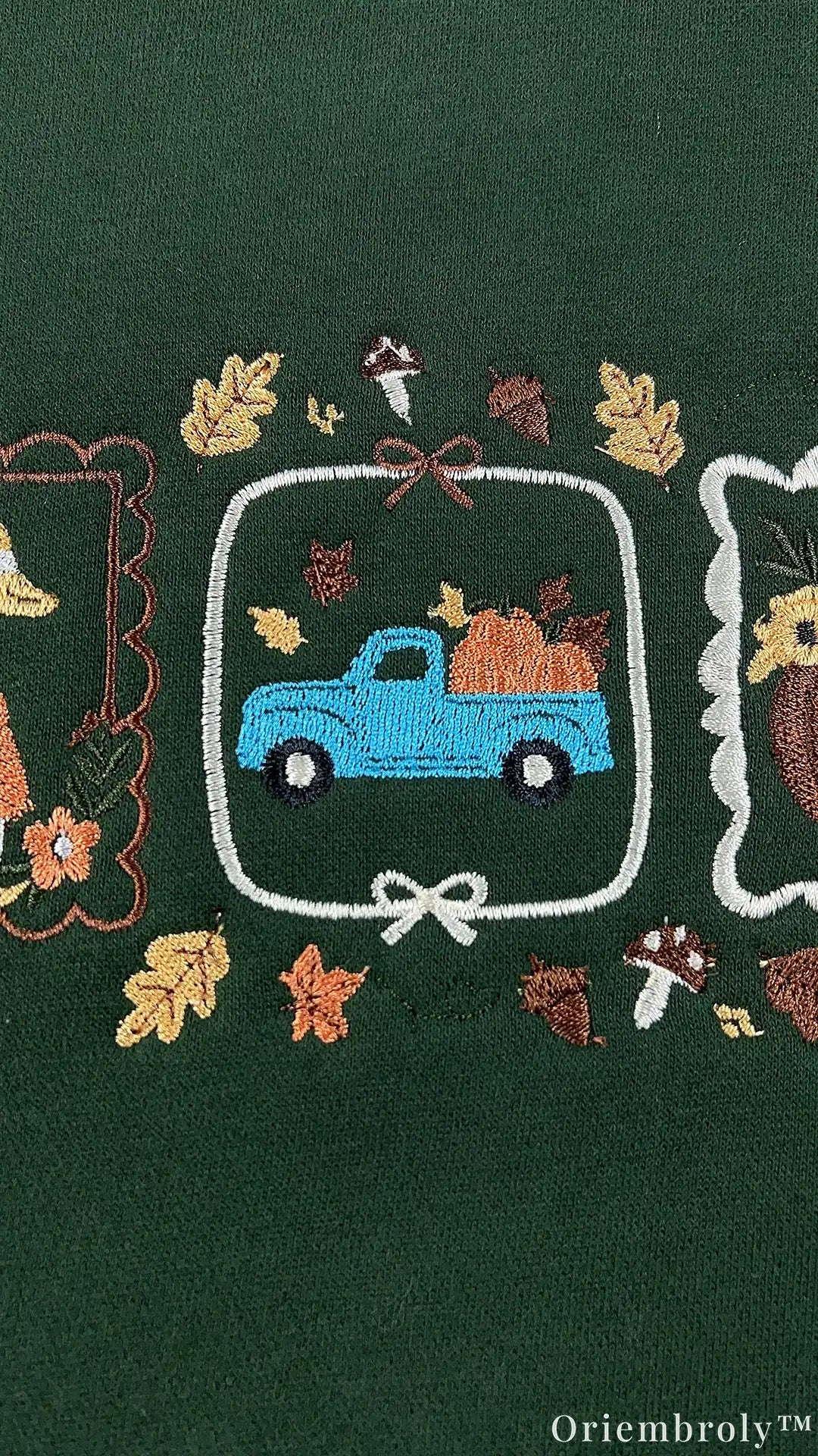 Close-up of embroidery featuring a vintage blue pickup truck loaded with orange pumpkins inside a white framed border on a green sweatshirt.