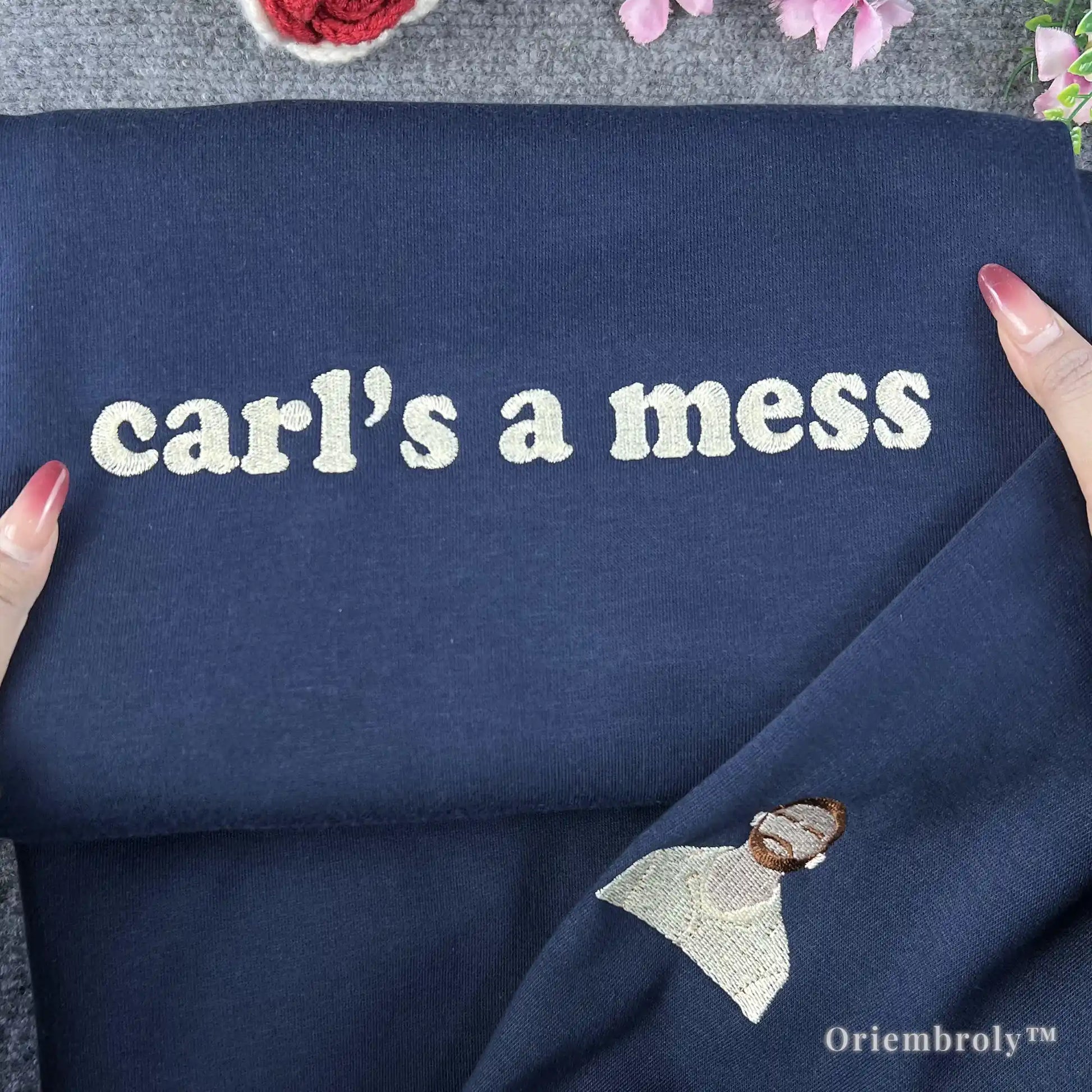 Navy blue pullover with a detailed embroidered character icon on the sleeve and "carl’s a mess" on the chest. High-density satin stitching inspired by viral internet characters and niche fandoms