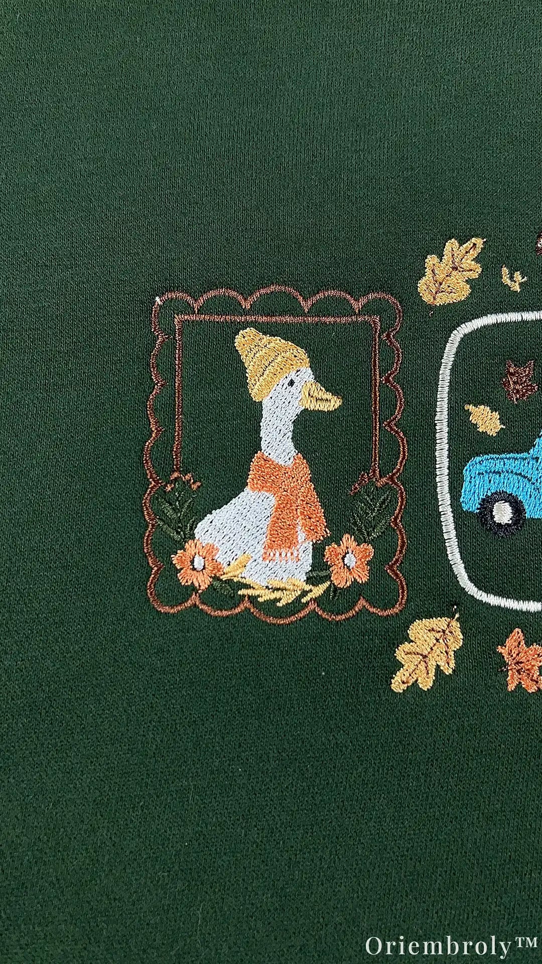 Close-up of fine embroidery showing a framed duck wearing an orange scarf and hat with autumn leaves on a green sweatshirt.