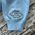 Light blue sweatshirt sleeve with embroidered design of two ducks and 'GOOSE BUMPS' text on a wooden surface.