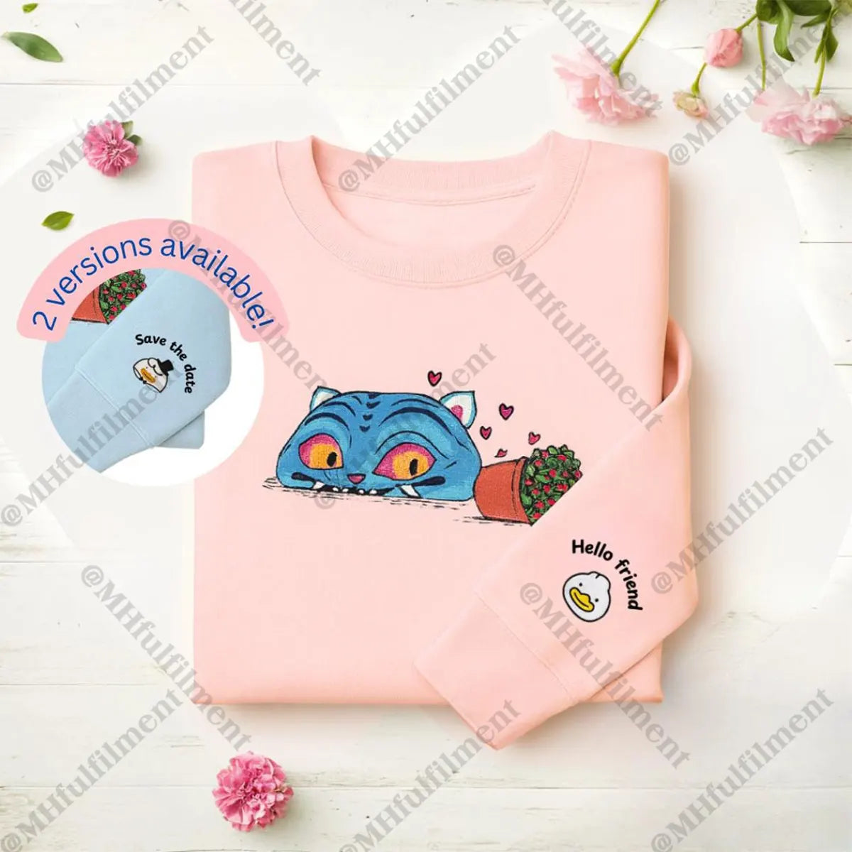 Pink shirt with cartoon cat design and small blue hat on a light wooden surface with flowers.