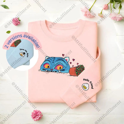 Pink shirt with cartoon cat design and small blue hat on a light wooden surface with flowers.