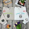 Two folded sweatshirts with embroidered designs on a wooden surface with flowers and a calendar.