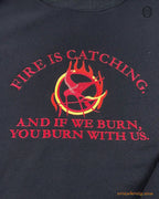 Close-up of red embroidered quote Fire Is Catching And If We Burn You Burn With Us with flaming Mockingjay symbol on a black sweater