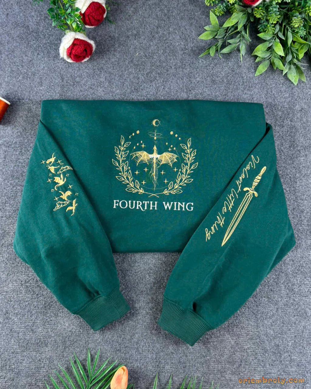 Flat lay of a forest green Fourth Wing sweatshirt featuring gold embroidered dragon, sword emblem, and detailed sleeve graphics