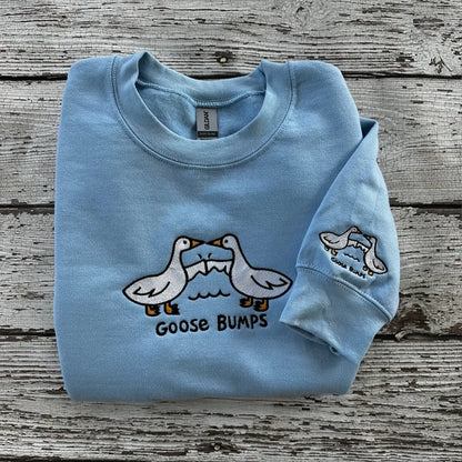 Light blue sweatshirt with goose design and 'Goose Bumps' text on a wooden surface