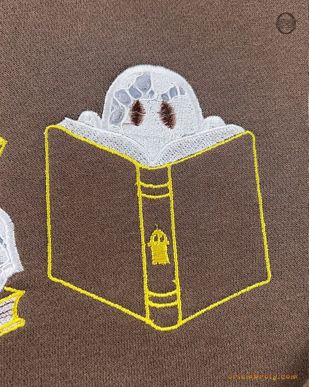 Close-up of a cute ghost hiding behind a giant open book embroidery detail on a brown sweatshirt