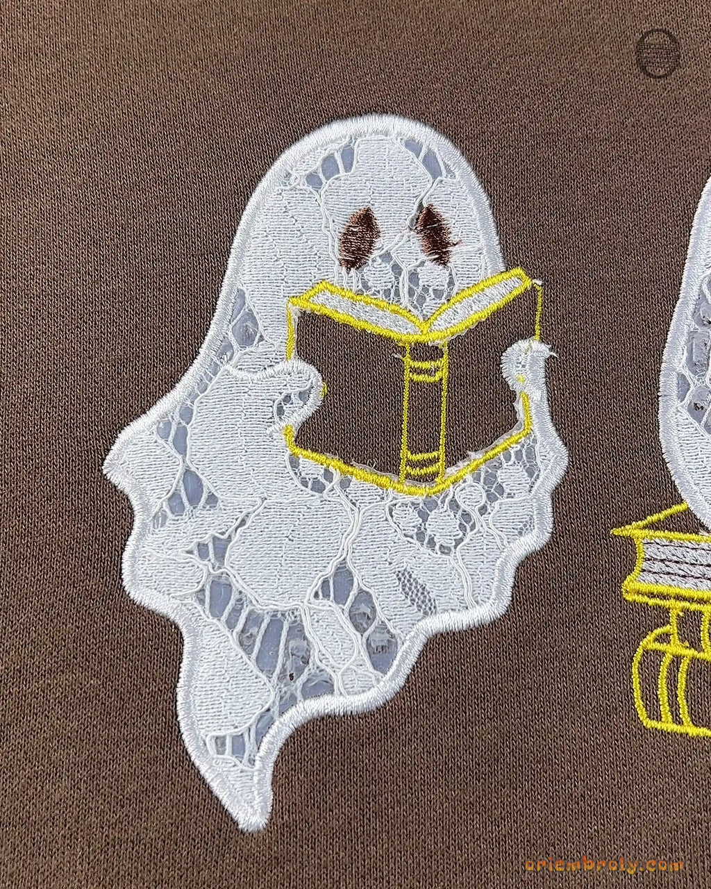 Close-up of a cute ghost holding and reading a open book embroidery on a brown sweater
